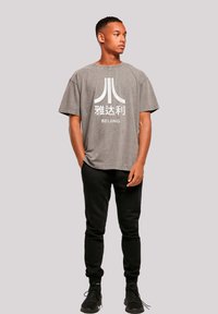 Graues, übergroßes T-Shirt mit einem weißen Grafikdesign und dem Text "Peking" auf der Vorderseite, kombiniert mit schwarzen Slim-Fit-Sweatpants und schwarzen Sneakers.