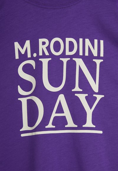Camiseta morada con texto impreso en blanco que dice "M. RODINI SUNDAY." Cuenta con un cuello redondo y una textura de tela suave y lisa.