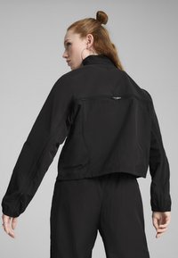 Črn skrajšan jakna, izdelana iz lahkega blaga, z dolgimi rokavi, visokim ovratnikom in zadrgo na hrbtni strani. Gladka tekstura in minimalističen dizajn.