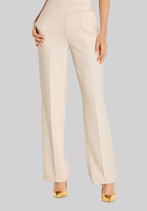 Beige hoge taille nette broek met voornaad, zijzakken, gedragen met gouden puntige hoge hakken op een lichtgrijze achtergrond.
