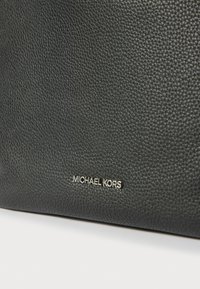 Čierna kožená taška s textúrovaným povrchom, na prednej strane s kultovým zlatým logom "MICHAEL KORS" a jemným, štruktúrovaným povrchom.