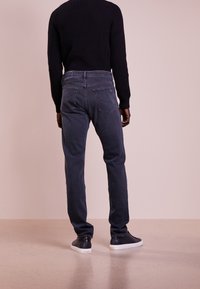Vaqueros de mezclilla gris de corte recto, con bolsillos traseros y costuras sutiles, combinados con zapatillas negras sobre un fondo claro.