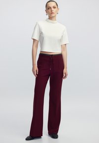 Wit cropped top met een hoge kraag, gecombineerd met bordeauxrode wijde pantalon met een koord in de taille en vo pockets. Textuur zwarte schoenen.