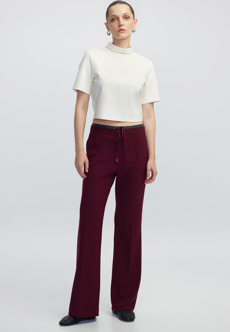 Wit cropped top met een hoge kraag, gecombineerd met bordeauxrode wijde pantalon met een koord in de taille en vo pockets. Textuur zwarte schoenen.
