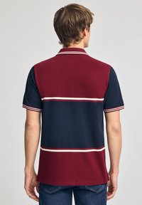 Kortärmad polo med maroon- och marinblå ränder, vita detaljer, ribbad krage och avslappnad passform. Mjuk bomullstyg.