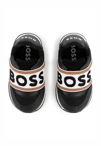 Black sneakers with mesh and synthetic material, featuring a wide elastic strap with "BOSS" lettering in white on a brown background.