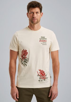 Cream-colored cotton T-shirt featuring red and green graphic prints and text on the front. Short sleeves, round neck, relaxed fit.