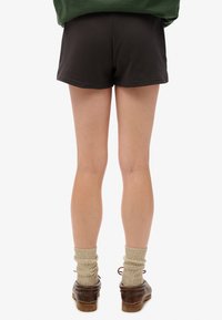 Shorts noirs à la texture lisse, vue arrière montrant l'ourlet et une coupe décontractée. Associés à des chaussettes en tricot beiges et des sabots marron.