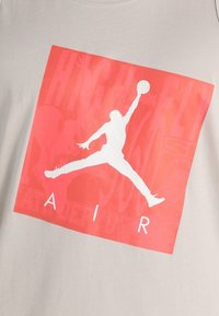 Silhuett av en basketspelare som hoppar med bollen i en röd fyrkant, med texten "AIR" nedanför på en ljusfärgad tygbakgrund.