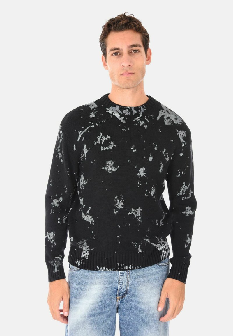 Maglione nero con motivi astratti grigi, polsini e orlo a coste. Indossato sopra jeans strappati blu chiaro. Girocollo.