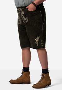 Svarta mockashorts med intrikata guldbroderier, sidoknappar och en skräddarsydd passform. Kombineras med bruna snörkängor och marinblå strumpor.