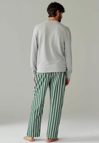 Harmaat pitkähihaiset paidat ja vihreät raidalliset pyjaman housut, joissa on valkoisia raitoja, näyttävät rentolta istuvuudelta ja pehmeältä kangasrakenteelta.