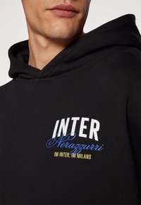 Moletom preto com um design gráfico em texto branco e azul que diz "INTER Nerazzurri IM INTER, IM MILANO" na parte da frente.