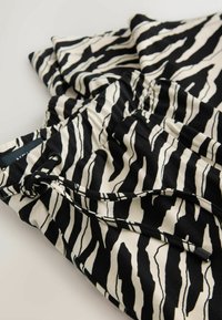 Čiernobiele pruhované nohavice so zebra vzorom a sťahovacím pásom, zobrazené zložené na svetlom povrchu.