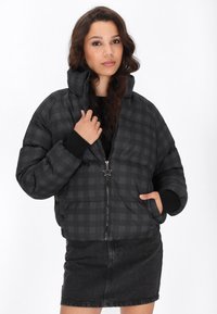 Černá kostičkovaná péřová bunda s kapucí a předním zipem, s hvězdicovým táhlem zipu. V kombinaci s černou džínovou sukní.