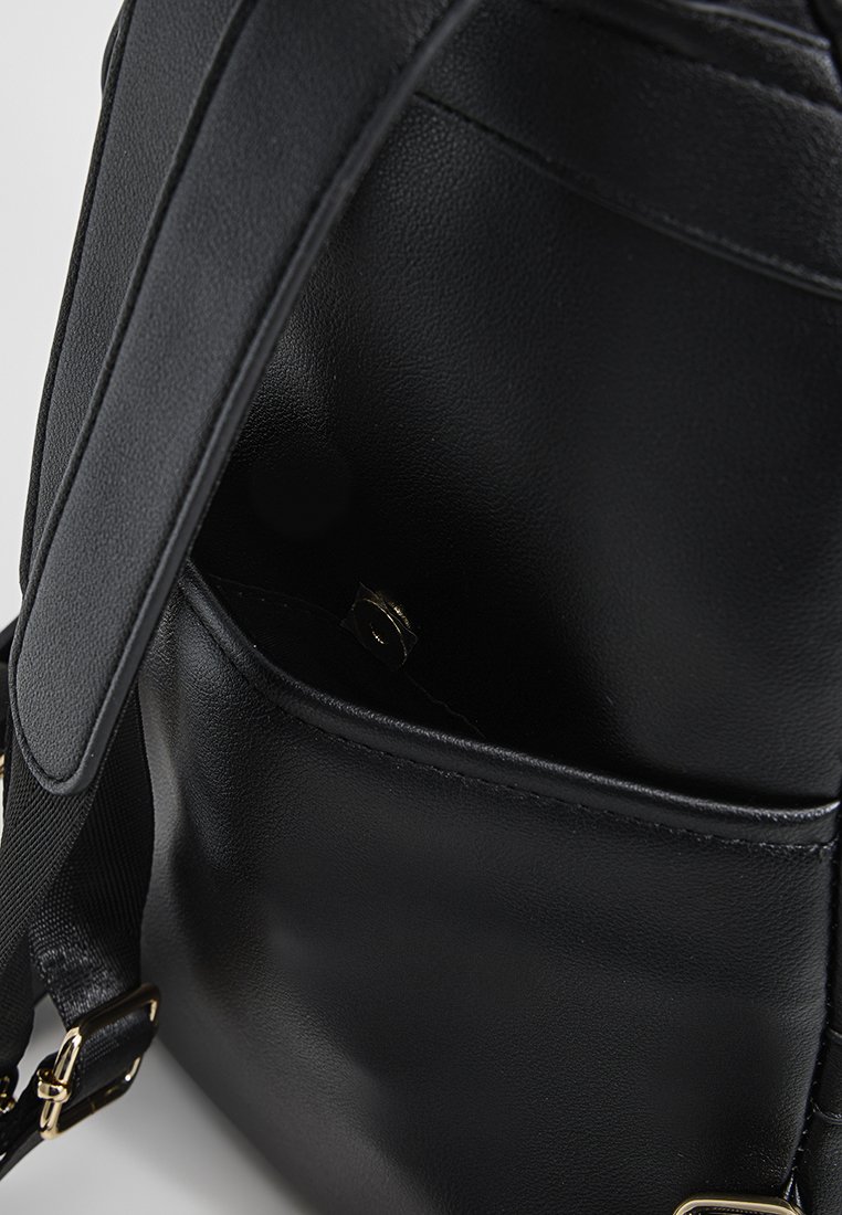 Schwarzer Leder-Rucksack mit glatter Textur, ausgestattet mit einer Seitentasche und goldenen Hardware-Akzenten. Verstellbarer Gurt für mehr Komfort.