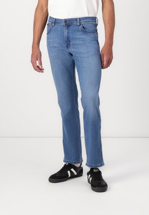 Blauwe denim jeans met een rechte snit, vijf zakken en subtiele vervagingen. Gecombineerd met zwarte sneakers met witte strepen.