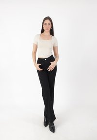 Top ajustado de cuello cuadrado beige con mangas cortas, combinado con jeans de campana negros de cintura alta y botas de tobillo negras con punta.