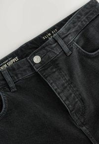 Blugi negri skinny din denim, cu închidere cu nasture, bucle pentru curea și buzunare frontale, având o textură moale și cusături subtile.