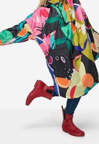 Färgglad, mönstrad regnponcho i svart, rosa, grön och gul; tillsammans med röda vattentäta ankstövlar med sidogummiband.