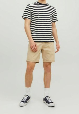 Gestreept marineblauw en wit katoenen T-shirt gecombineerd met beige korte broek. Witte enkelsokken en marineblauwe sneakers maken de casual look compleet.