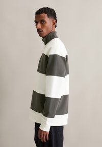 High-neck, zippered sweatshirt with vertical stripes in white and dark green. Features ribbed cuffs and a relaxed fit. Soft fabric texture.