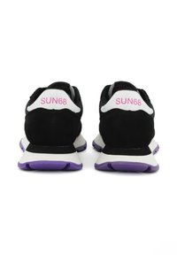 Een paar zwart-witte sneakers met paarse zolen, het "SUN68" logo in het roze aan de achterkant, getoond vanuit de achterzijde.