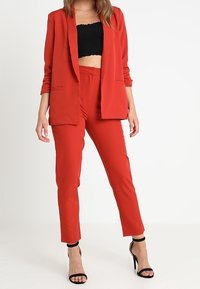 Czerwony dopasowany żakiet i pasujące wąskie spodnie, zestawione z czarnym krótkim topem, wykończone czarnymi szpilkami na kostkę.