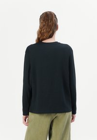 Black long-sleeve shirt with a crew neckline, made of soft fabric, paired with light green corduroy pants featuring vertical stripes.