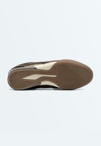 Semelle d'une basket marron et beige avec un motif de grip texturé et le nom de la marque "Oysho" embossé près de la voûte plantaire.