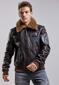 Veste bomber en cuir marron avec un col en fausse fourrure, fermeture éclair, poignets côtelés, une poche sur la poitrine et des poches latérales. Design texturé et ajusté.