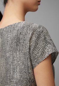 Haut noir et blanc à motifs avec des manches courtes, présentant un tissu texturé et une coupe ample. Le design est composé de lignes ondulées sur un fond clair.