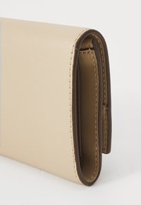 Portefeuille en faux cuir beige avec une texture lisse, des accents marron et des coutures visibles le long des bords. Design plié avec des coins arrondis.