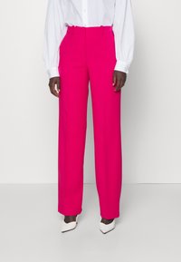 Heldere roze, wijde broek in een gladde stof. Kenmerkt zich door een hoge taille met riemlussen, zijzakken en een strakke, getailleerde uitstraling.