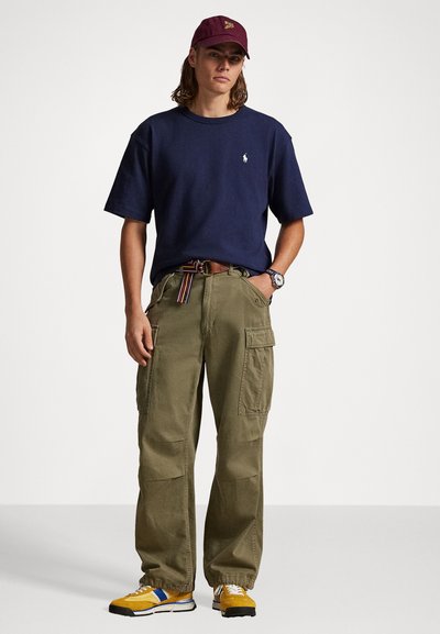 Ναυτικό βαμβακερό μπλουζάκι, ελιές cargo παντελόνια με πλαϊνές τσέπες, κίτρινα και μπλε αθλητικά παπούτσια. Αξεσουάρ περιλαμβάνουν ένα μπορντό καπέλο και ρολόι.