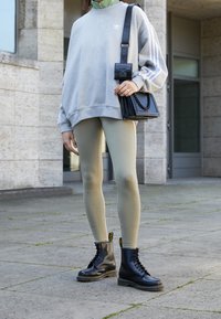 Grå överdimensionerad sweatshirt med vita ränder, ljusgröna leggings, svarta snörboots och en texturerad svart handväska med kedjedetaljer.