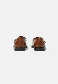 Un paio di scarpe eleganti in pelle marrone con suole nere, viste da dietro su uno sfondo bianco semplice.