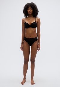 Σετ μαύρο σουτιέν με λεπτομέρειες από δαντέλα και μαύρο στρινγκ που ταιριάζουν. Μαλακό ύφασμα, μη επενδεδυμένα cups, ρυθμιζόμενες τιράντες και απαλό ύφος. Απλός σχεδιασμός.