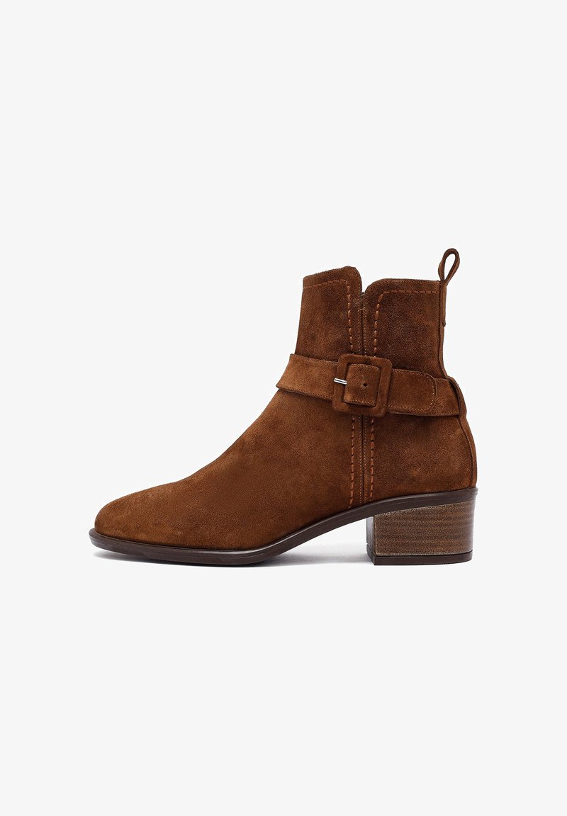 Stivale ankle in suede marrone con punta arrotondata, dettaglio con fibbia laterale, accenti cuciti e tacco medio in legno.