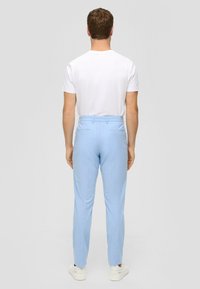 Světlé modré kalhoty na míru s hladkou texturou, přizpůsobeným střihem a zadními kapsami, doplněné jednobarevným bílým tričkem a bílými teniskami.