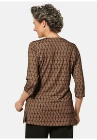 Braun gemustertes Oberteil mit geometrischen Designs, Dreiviertelärmeln und rundem Ausschnitt. Leicht längerer Rücken mit seitlichen Schlitzen.