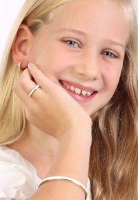 Een meisje met lang blond haar draagt zilveren oorbellen en een dunne zilveren ring. Een eenvoudige zilveren armband accentueert haar pols.
