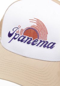 Biely čiapka s béžovým okrajom, s fialovým vyšívaným nápisom "Ipanema" a kruhovým oranžovým grafickým motívom s vlnitými čiarami. Texturovaný sieťovaný zadok.