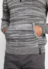 Suéter de punto a rayas gris y negro con cuello redondo, mangas largas, bolsillos delanteros y puños y dobladillo acanalados texturizados.