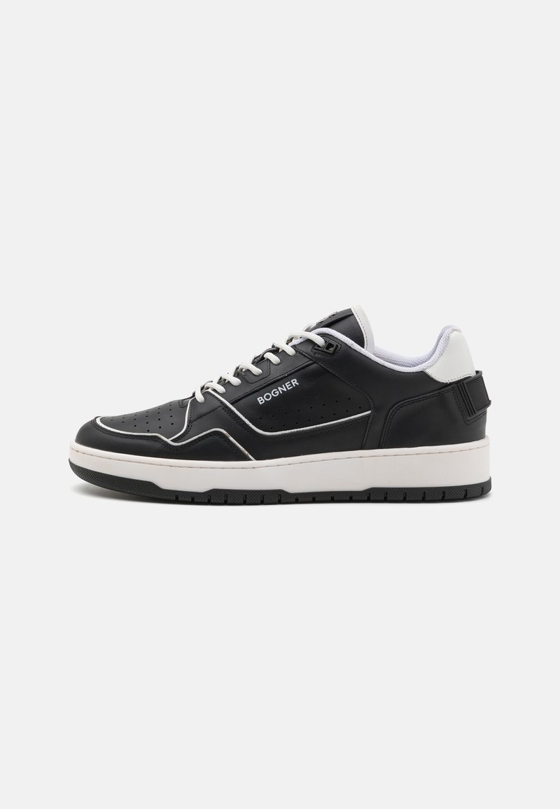 Black sneaker with white accents, smooth leather upper, perforated details, round toe, and thick white sole. Branding visible on the side.