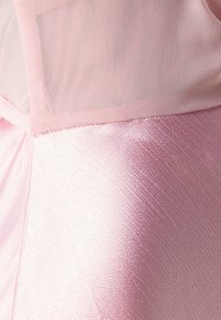 Ružové šaty s textúrovanou saténovou spodnou časťou a priehľadnou sieťovinou v hornej časti. Majú jemný lesk a delikátne švy.