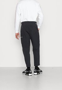 Svarta cargobyxor med smalnande ben, elastisk midja och sidofickor. Bärs med en vit sweatshirt och svarta sneakers med vita detaljer.