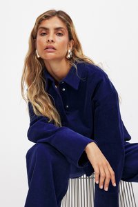 Navy corduroy shirt and pants set with a collared neckline, button details, and textured fabric. Model wears large metallic hoop earrings.