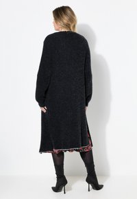 Kardigan panjang hitam dengan rajutan berpola, bagian depan terbuka, dan belahan samping. Dipadukan dengan gaun floral dan sepatu bot hak tinggi hitam.