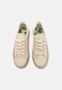 Zapatillas de lona beige con punta redonda, superficie texturizada y detalles de yute trenzado en la suela. Patrón tropical colorido en la plantilla.